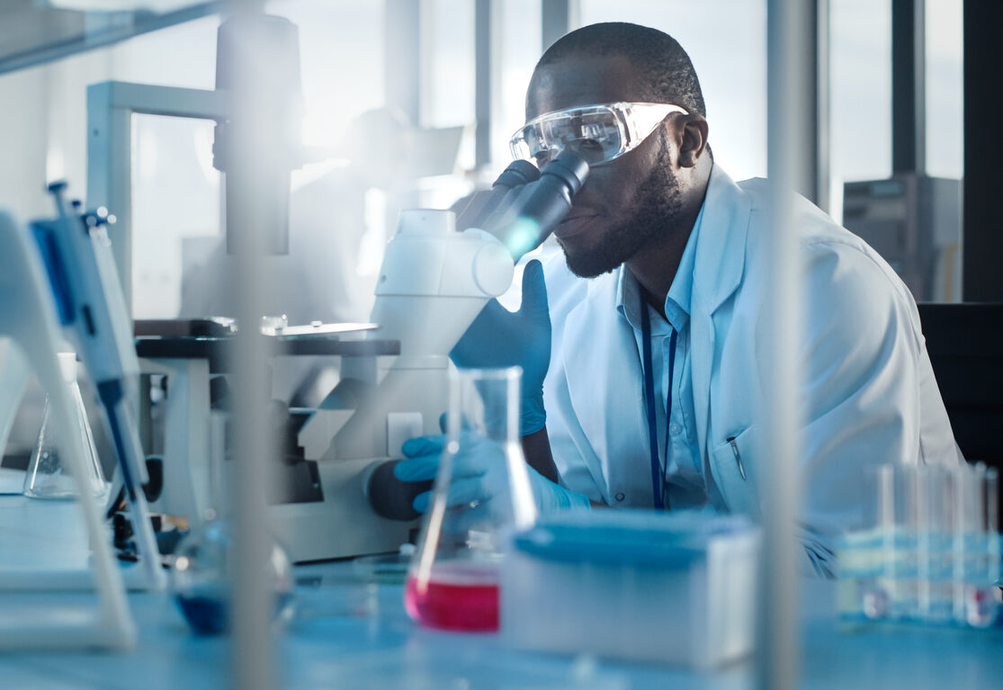 Medical Development Laboratory: Black Male Scientist Looking Under Microscope, Inspecting Petri Dish. Professionals Working in Advanced Scientific Lab doing Medicine, Vaccine, Biotechnology Research