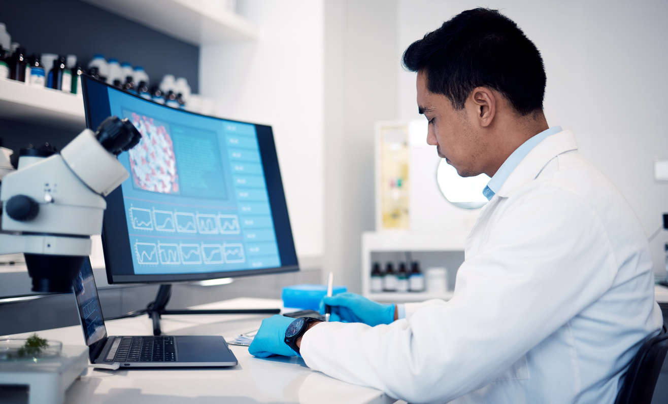 Man, scientist and computer with virus, bacteria and research data in laboratory. Science worker writing notes on vaccine, development or dna on technology, digital analytics or pharmaceutical health