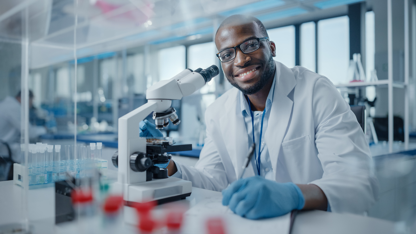 Modern Medical Research Laboratory: Portrait of Male Scientist Using Microscope, Charmingly Smiling on Camera. Advanced Scientific Lab for Medicine, Biotechnology, Microbiology Development